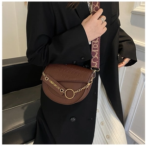 Detail einer braunen Satteltasche mit Krokodilmuster, Goldkette und Web-Schultergurt