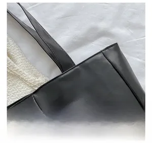 Detail shot of precise stitching on a large black matte leather tote bag with a white background