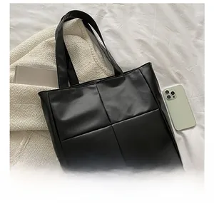 Detailed view of large quilted black tote bag with shoulder straps and smartphone for scale