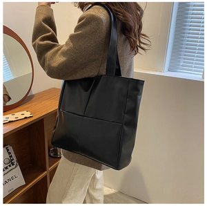 Detailed shot of a black matte PU leather tote bag worn on shoulder in a cozy room