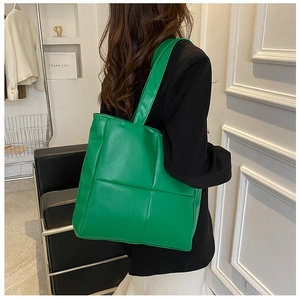 Detail of a bright green large capacity tote bag worn by a model in a modern interior setting