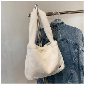 Close-up of white plush shoulder bag featuring soft faux fur texture and silver metal badge