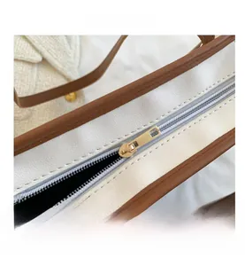 Detail view of smooth golden metal zipper on a two-tone white and brown tote bag