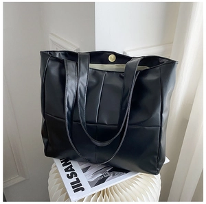 Close-up of large black quilted tote bag showing top magnetic closure and glossy PU leather