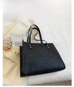 Detail of black PU leather tote bag with embossed graffiti pattern and gold metal rivets