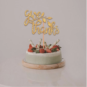 Close-up of golden Give Thanks glitter cake topper with leaf details on a fresh cake