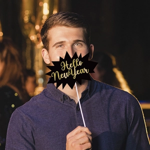 Black and gold Hello New Year photo booth prop held by man with festive bokeh lights