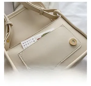 Detail view of round metal magnetic buckle and precise stitching on beige square bag