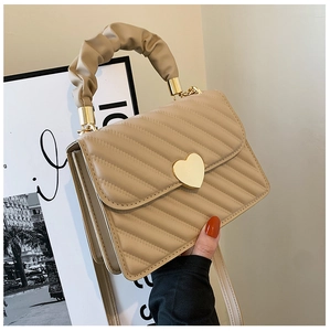 Detalle de bolso acolchado beige con cierre de corazón dorado y asa fruncida
