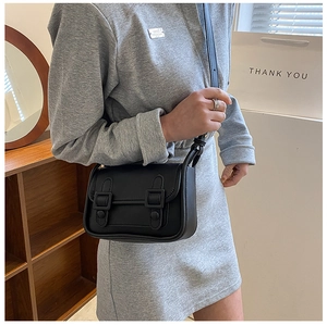 Close-up of a vintage black leather crossbody bag with double buckle flap worn by a model