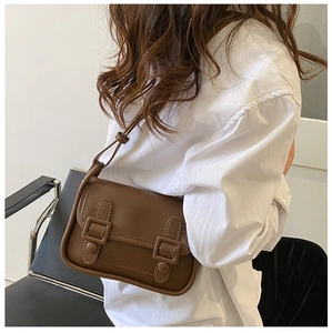 Close-up of a vintage brown leather crossbody bag styled with a white shirt and black pants