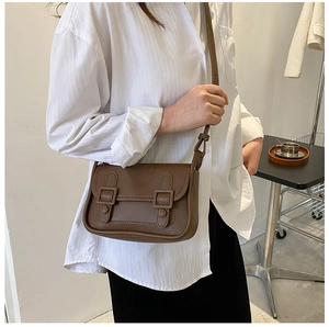 Retro brown leather crossbody bag with double buckle flap shown on model in minimalist room