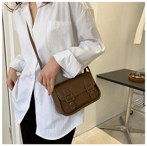 Detail of vintage brown shoulder bag showing buckle flap and leather texture on a model