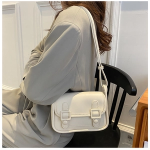 Close-up of cream shoulder bag featuring dual decorative buckles on the front flap