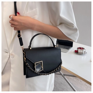 Detail of black matte handbag with gold geometric buckle on a white suit background