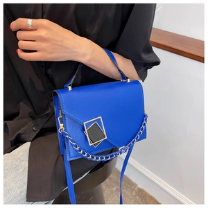 Detail of royal blue flap bag featuring geometric gold buckle and metallic chain strap