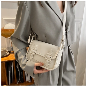 Detail of cream minimalist crossbody bag with double buckle straps on a model