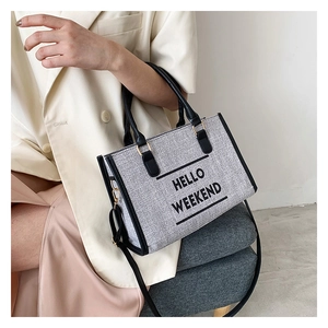 Detail of grey woven tote bag featuring black HELLO WEEKEND print and leather handles