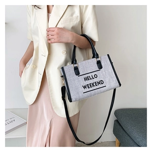 Detail of grey canvas tote bag featuring black HELLO WEEKEND text and leather handles