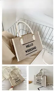 Close-up of beige canvas tote with HELLO WEEKEND text and white leather handles