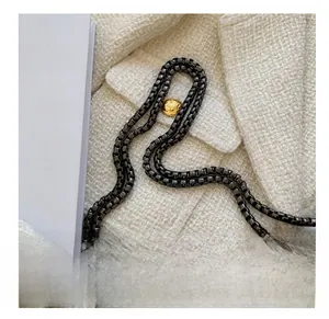 Detail of black quilted leather handbag with gold lion emblem clasp and dark chain