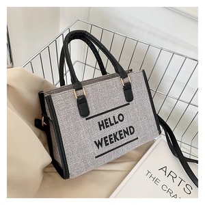 Detail of grey canvas tote bag featuring Hello Weekend print and black leather handles