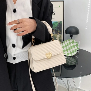Elegante bolso de mano crema con diseño acolchado y gran cierre de corazón dorado de hombro