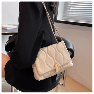 Détail du sac matelassé blanc à chaîne et fermoir doré sur une veste noire