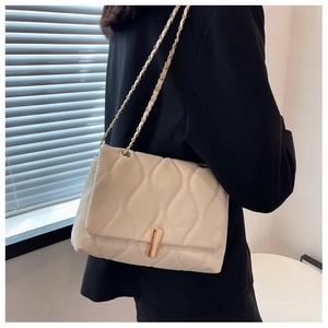 Détail du sac matelassé crème avec boucle dorée porté sur un blazer noir chic