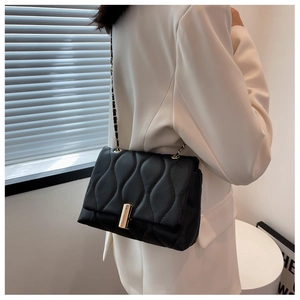 Détail d'un sac à chaîne matelassé noir porté à l'épaule sur un blazer beige
