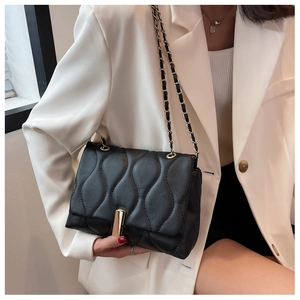 Détail d'un sac bandoulière noir matelassé avec chaîne dorée sur veste blanche