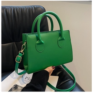 Close-up of small emerald green leather handbag with gold hardware on a black leather chair
