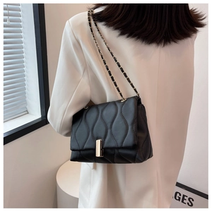 Détail du sac bandoulière noir avec matelassage ondulé, boucle dorée et bandoulière
