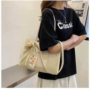 Dettaglio della borsa a secchiello intrecciata beige con fiocco di pizzo e ricami floreali