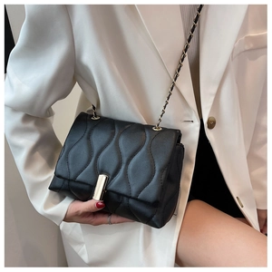 Gros plan du sac bandoulière noir matelassé avec chaîne dorée porté sur un blazer blanc
