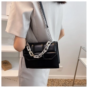 Détail d'un sac à bandoulière matelassé noir avec chaîne argentée, porté par un mannequin