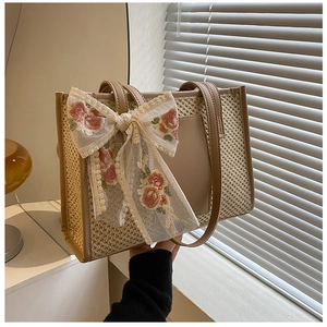 Dettaglio della borsa tote in paglia con fiocco in pizzo floreale e rifiniture in pelle