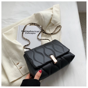 Détail du sac matelassé noir avec chaîne dorée sur fond de veste de tailleur blanc