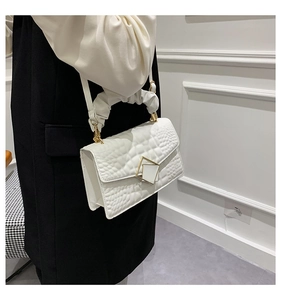 Gros plan sur un sac blanc motif crocodile avec boucle dorée et poignée à volants