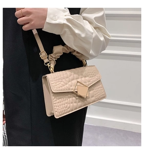 Détail d'un sac beige effet crocodile avec fermoir doré et poignée souple plissée