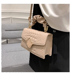Détail du sac bandoulière beige avec texture crocodile et poignée nuage sur un fauteuil chic