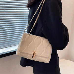Sac bandoulière matelassé beige chic avec chaîne porté sur un blazer noir