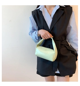 Detail view of a soft light green cylindrical leather handbag with a minimalist handle