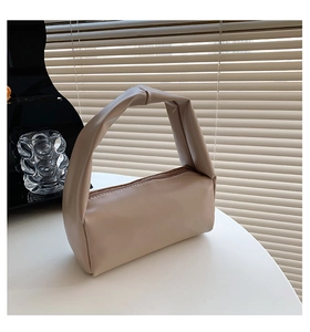 Detail of beige faux leather handbag with unique twisted handle and zipper closure