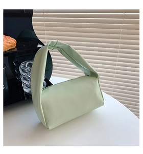 Chic mint green soft leather handbag with knot handle detail on a stylish desk setting