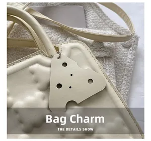 Close-up of cream faux leather handbag featuring embossed texture and geometric charm detail