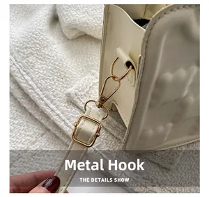 Detail of the golden metal hook and adjustable leather strap on a cream biscuit bag