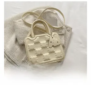 Detail view of cream biscuit texture crossbody bag with mini cheese charm and phone for scale