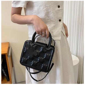 Detail of black leather handbag with embossed bear patterns and cheese-shaped charm