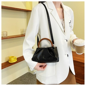 Detail of black pleated cloud bag featuring a round wooden handle and a detachable strap